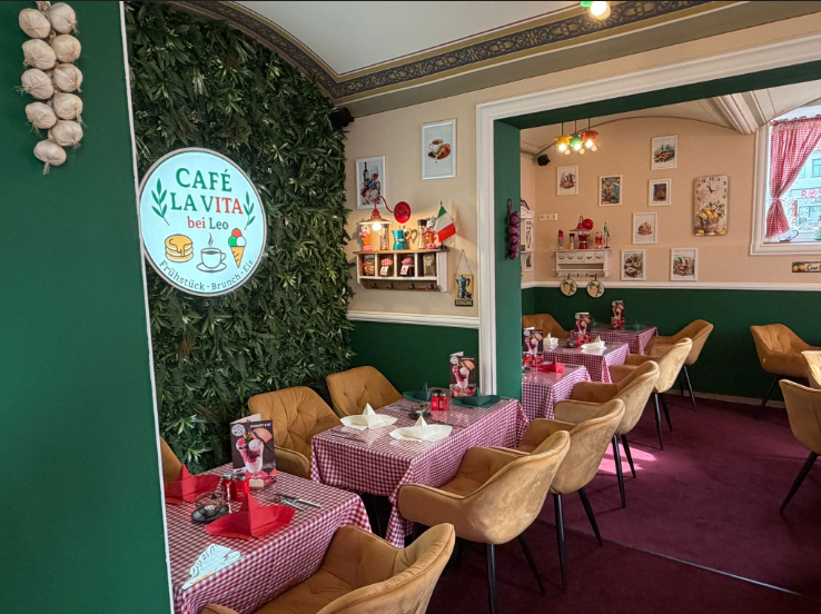 Café La Vita Speisesaal mit Logo-Wand und rot karierten Tischdecken.